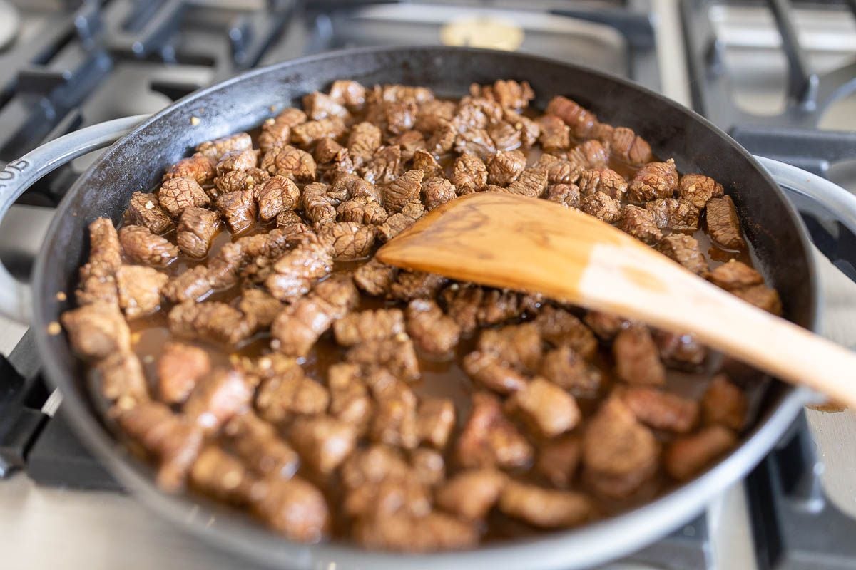 marinated carne asada street taco steak, cooking in a cast iron pan.