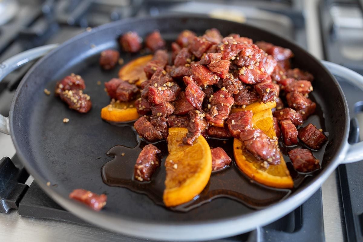 marinated carne asada street taco steak, cooking in a cast iron pan.