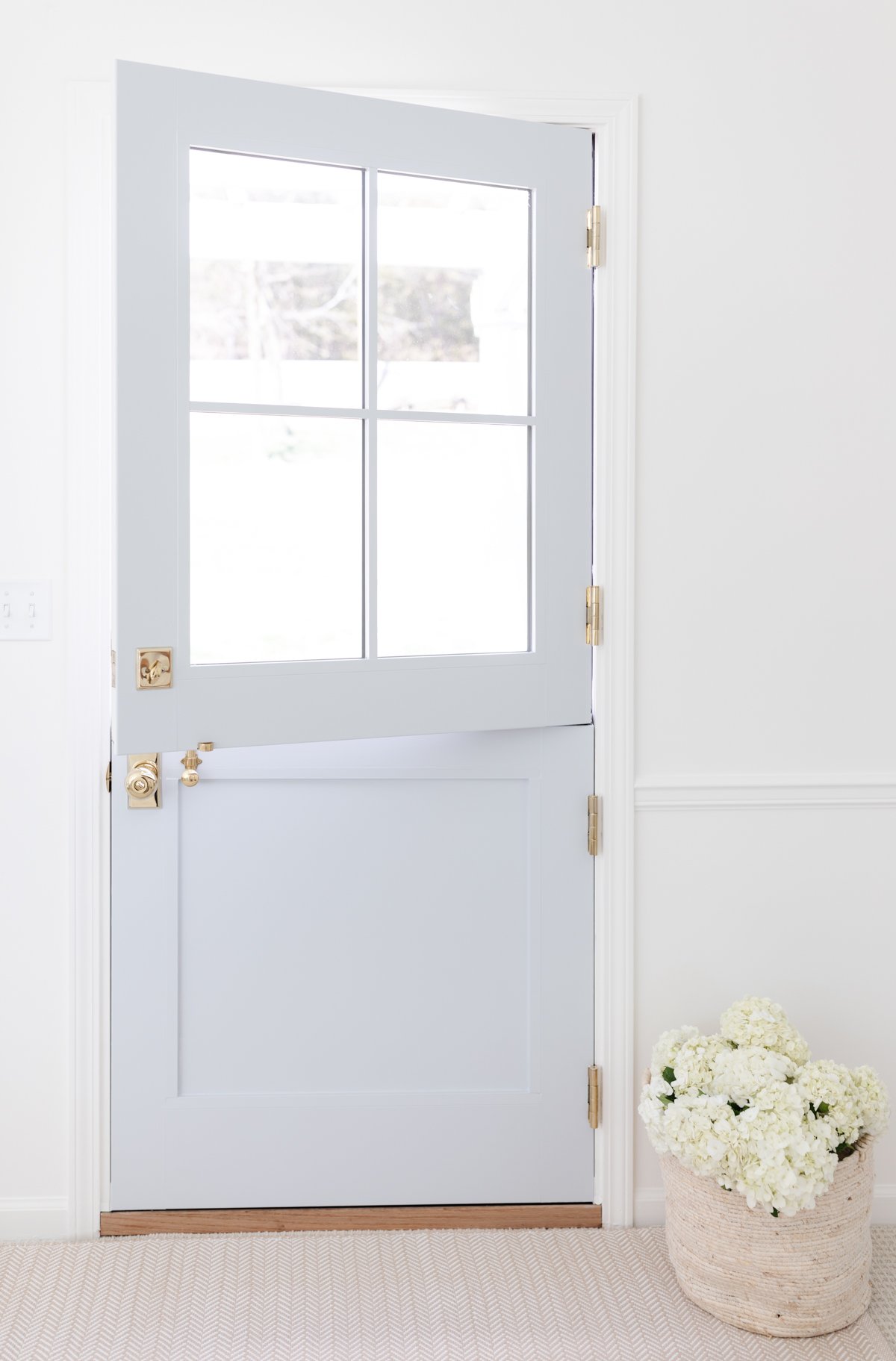 A soft blue dutch door with a neutral indoor outdoor rug in front.