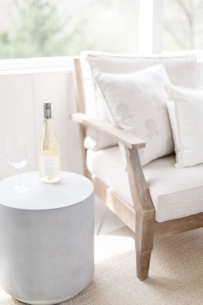 A white screened in porch with a wooden chair and a round side table