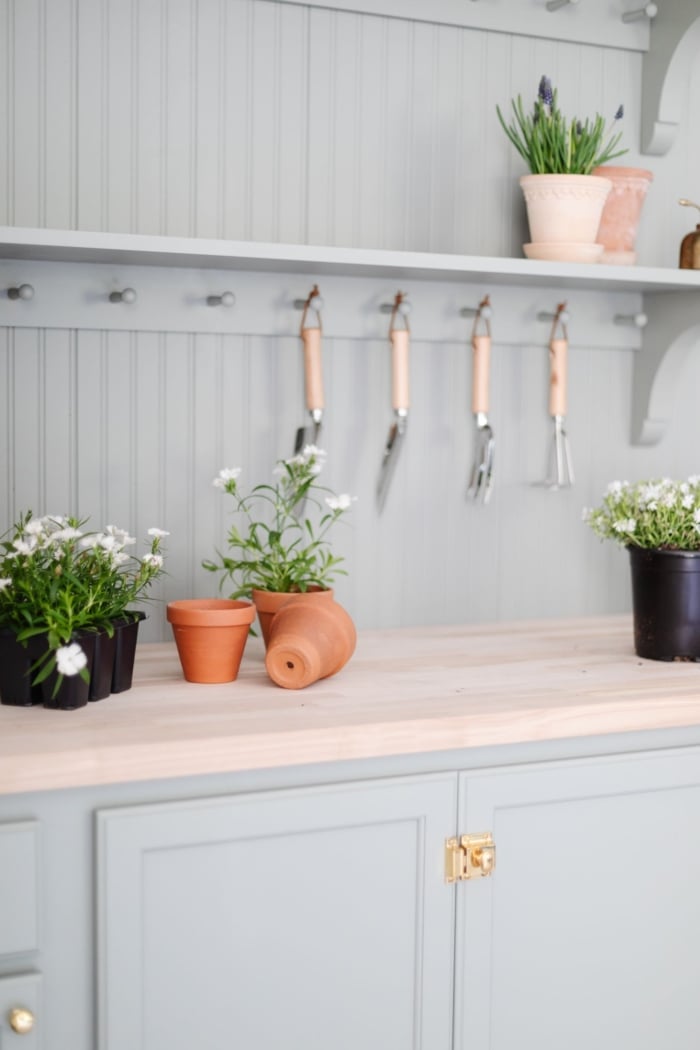 A potting bench painted in a green gray color, flowers and tools on top