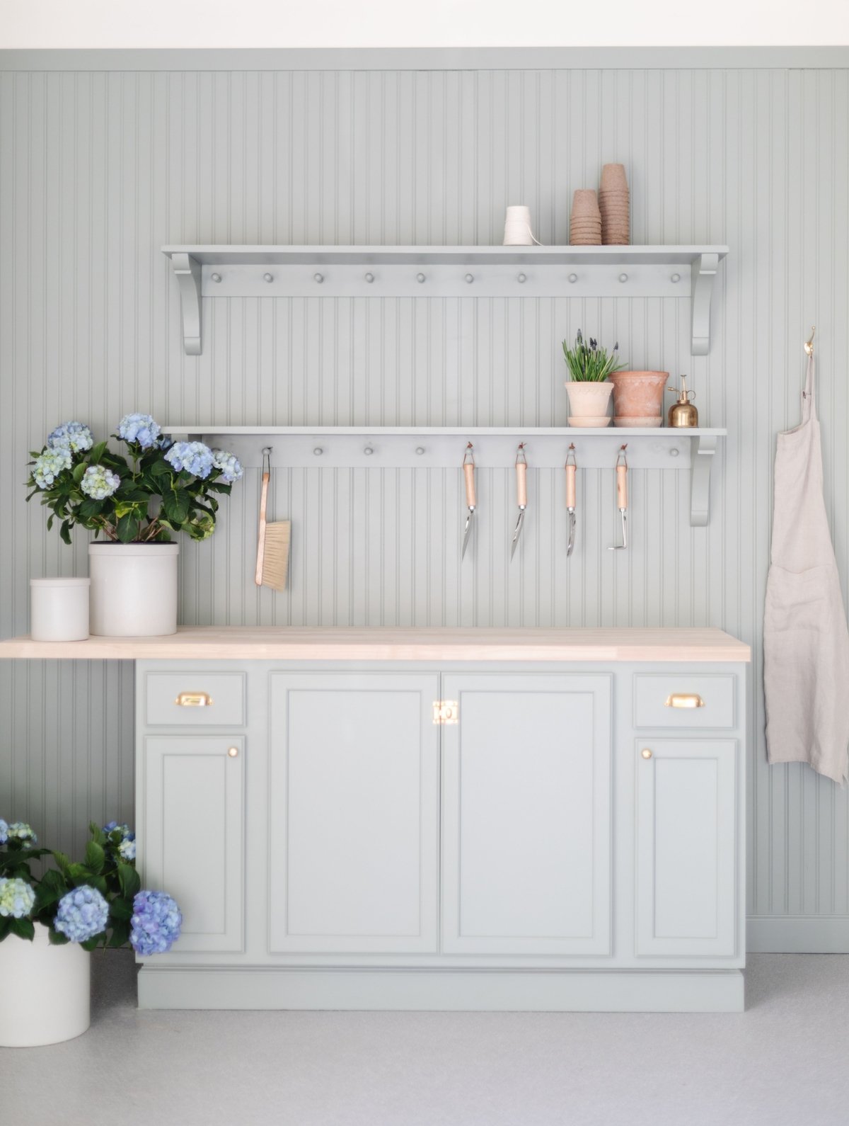 A potting bench painted in a green gray color, flowers and tools on top