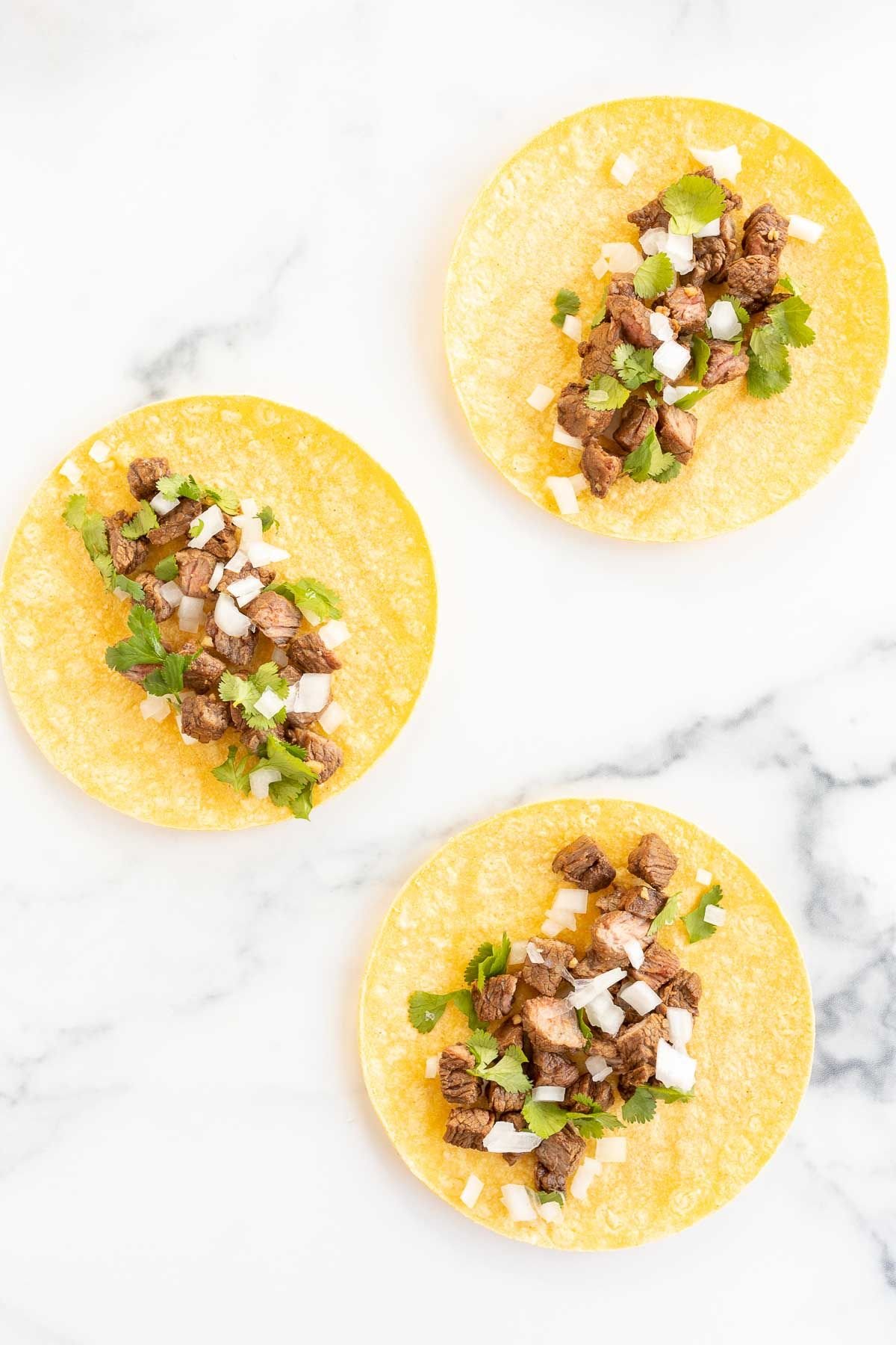 Carne asada street tacos in corn tortillas laid out flat on a marble surface