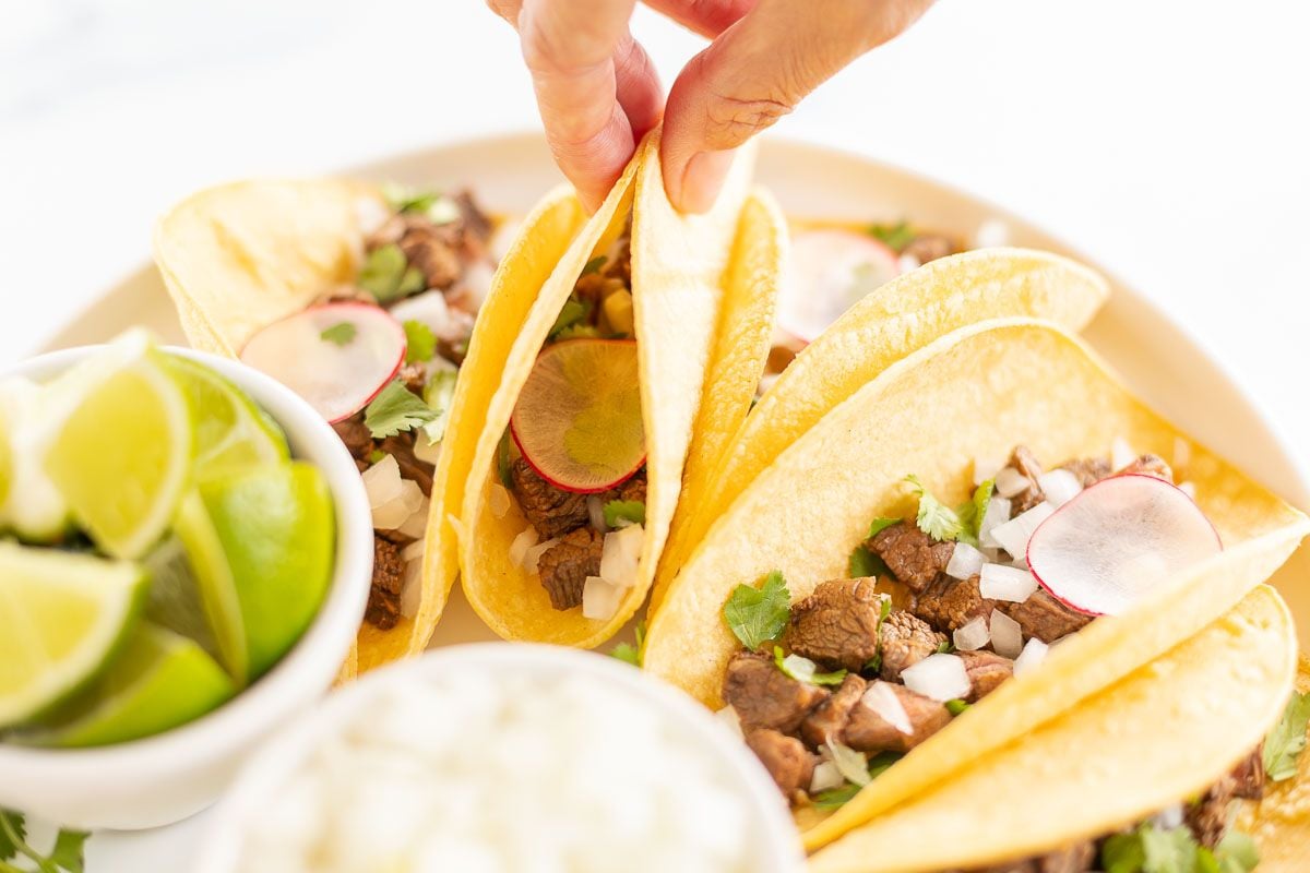 Street tacos on a white platter with a bowl of sliced limes and sliced onions