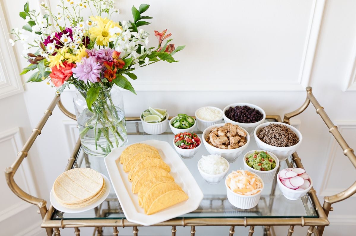 A taco bar display with flowers on a gold bar cart