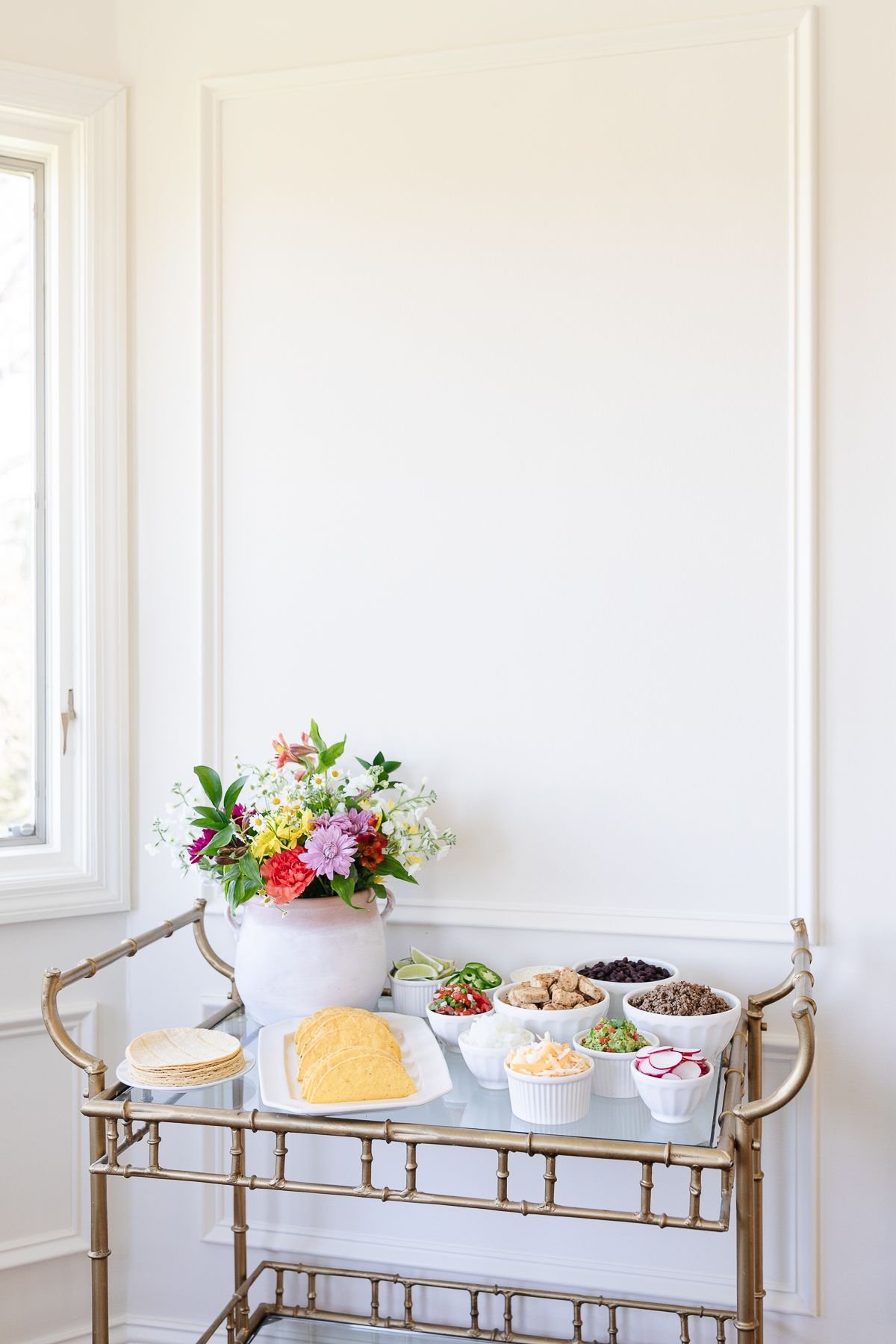 A taco bar display with flowers on a gold bar cart