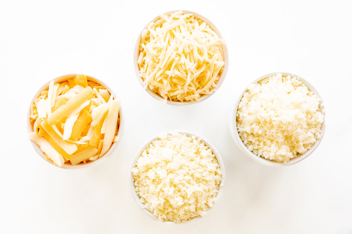 Four bowls of Mexican cheese on a white surface.