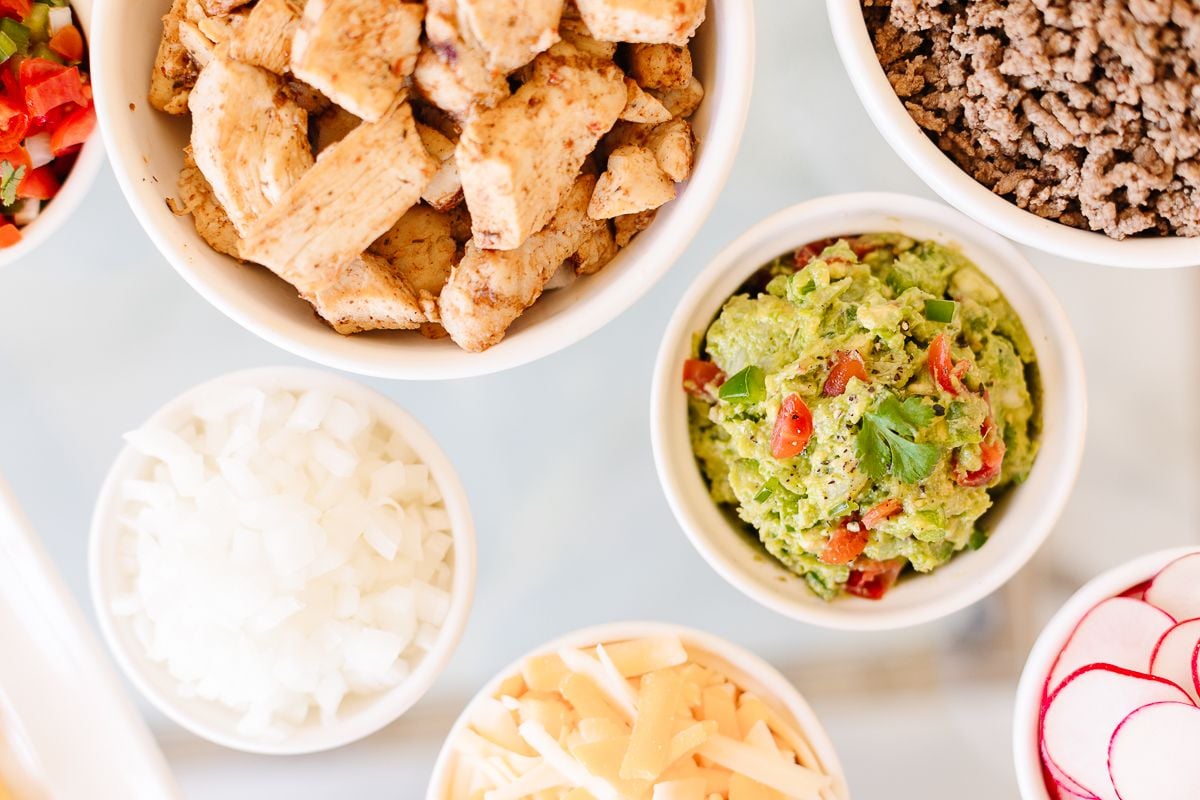 taco meat and taco toppings in white bowls on a white surface