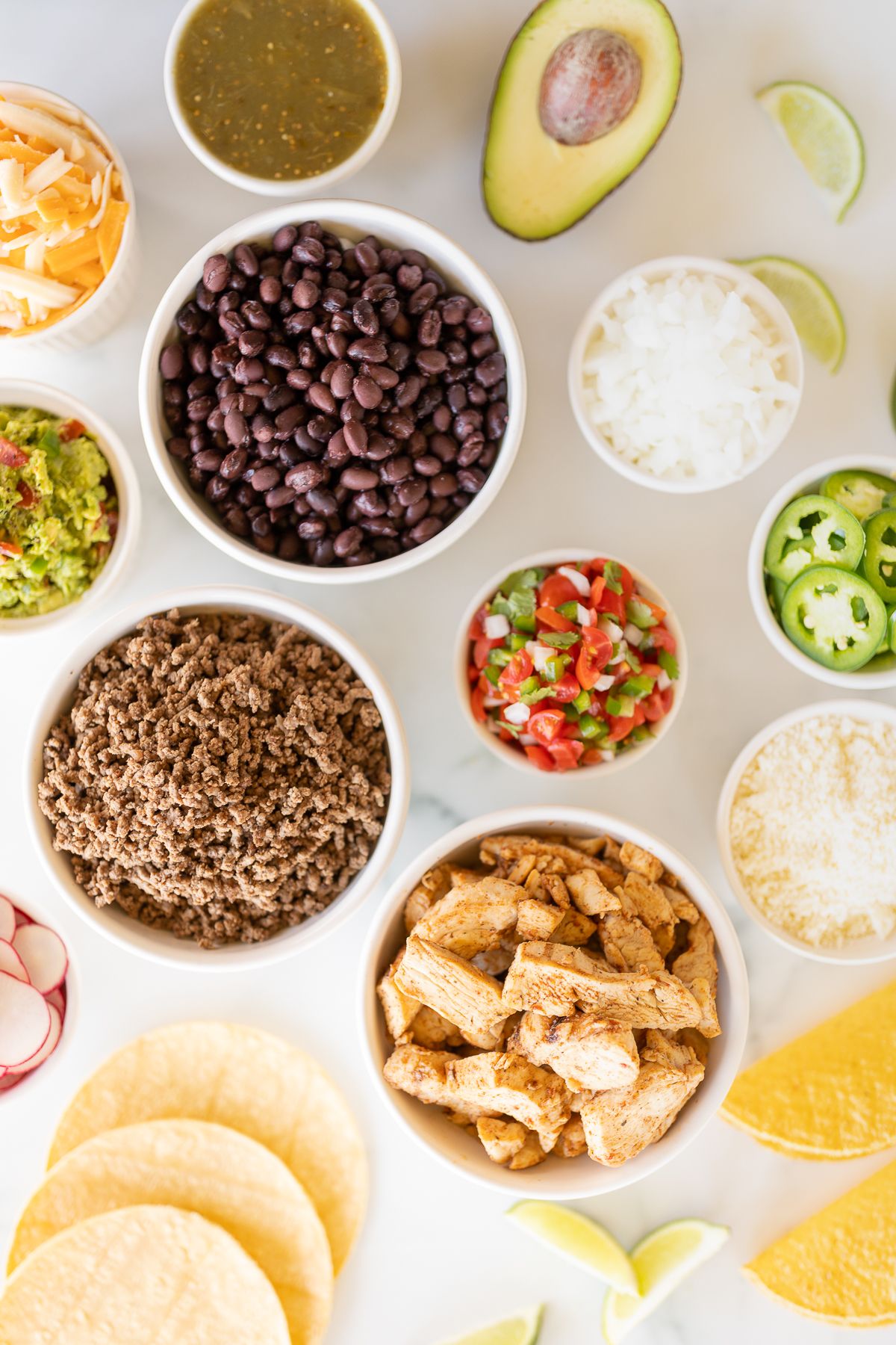 A display of taco toppings on a white marble countertop