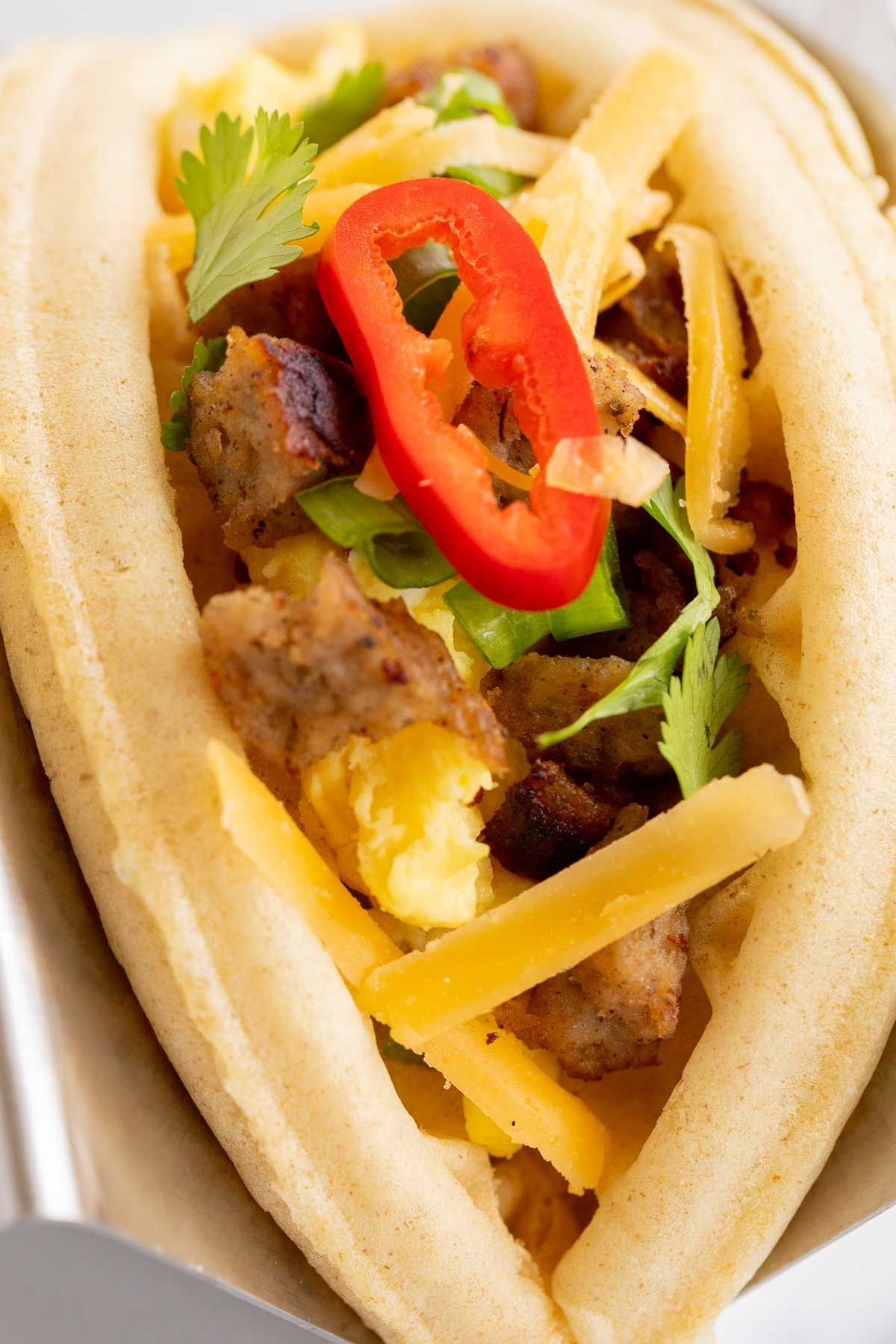 A waffle taco for breakfast, filled with eggs, sausage and traditional taco toppings