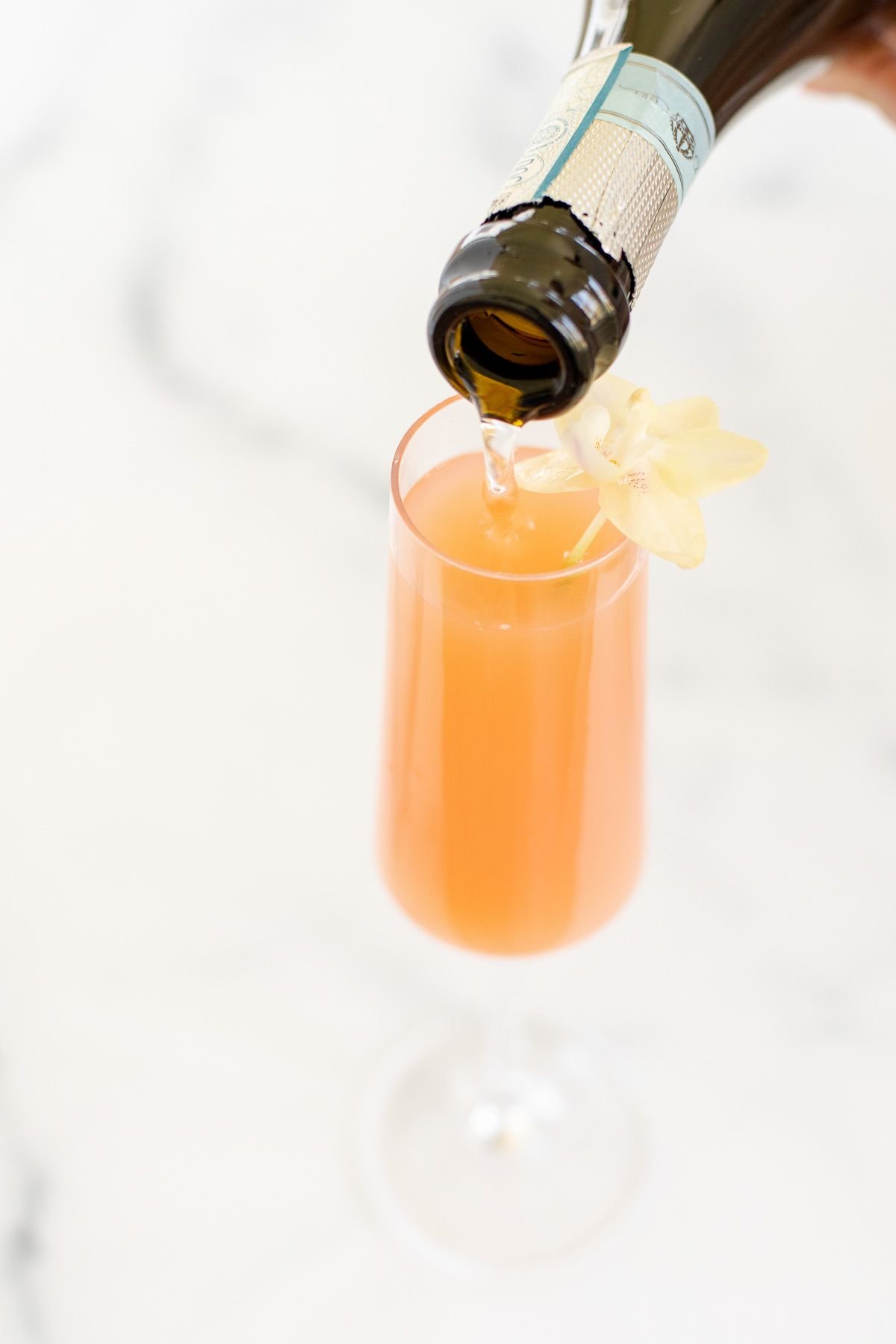 prosecco being poured into a mimosa on a marble surface