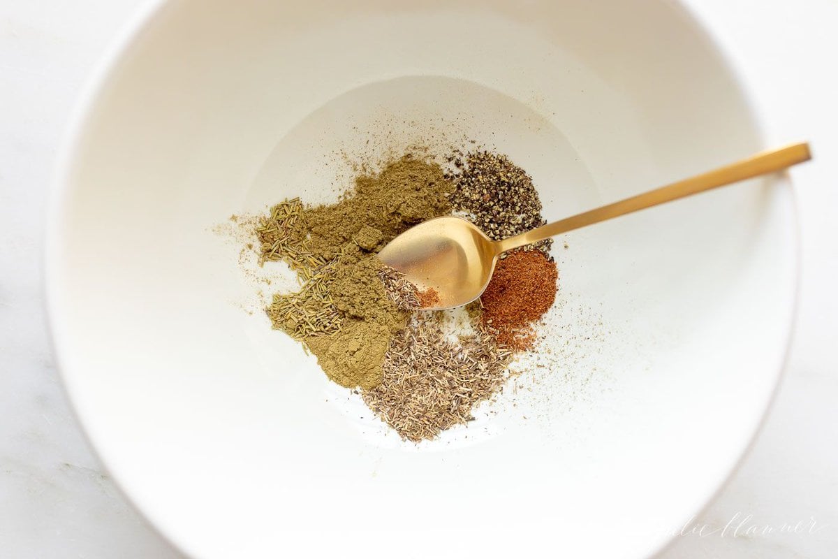 A chicken seasoning blend in a white bowl with a gold spoon