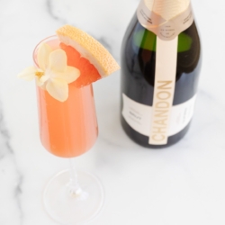 A grapefruit paloma on a marble surface, bottle of champagne to the side