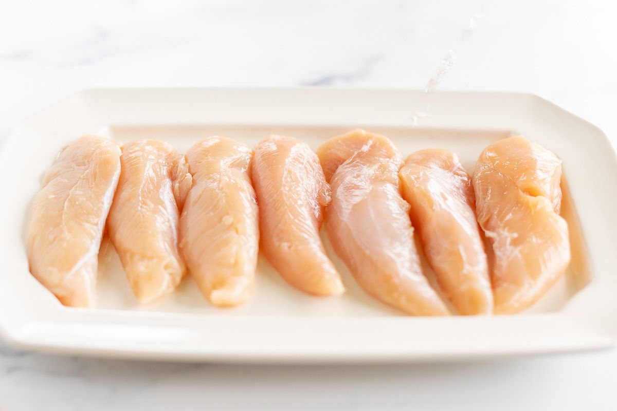 Chicken tenders, uncooked, on a white platter