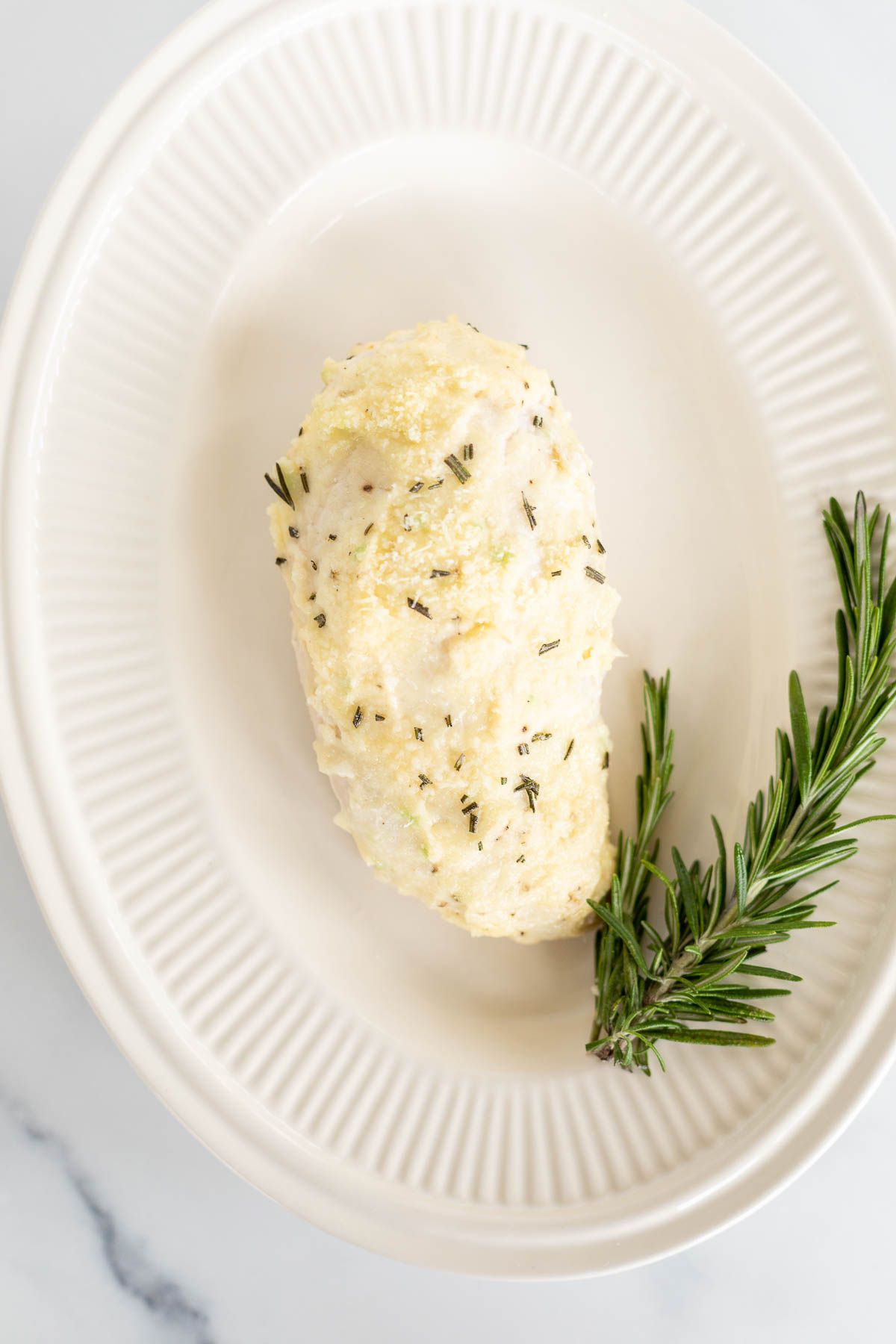 Mayo chicken, garnished with fresh rosemary on an oval platter.