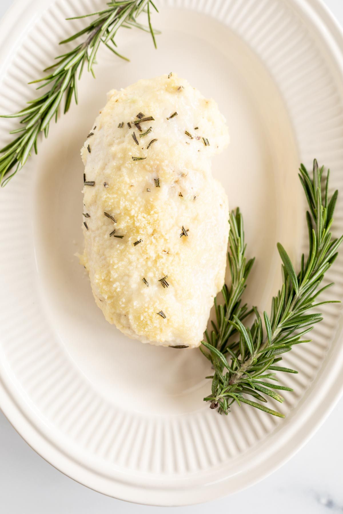Mayo chicken, garnished with fresh rosemary on an oval platter.