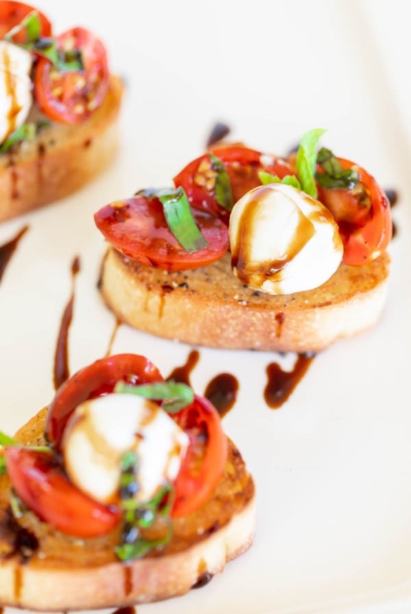 Bruschetta with mozzarella on crostini, on a white platter