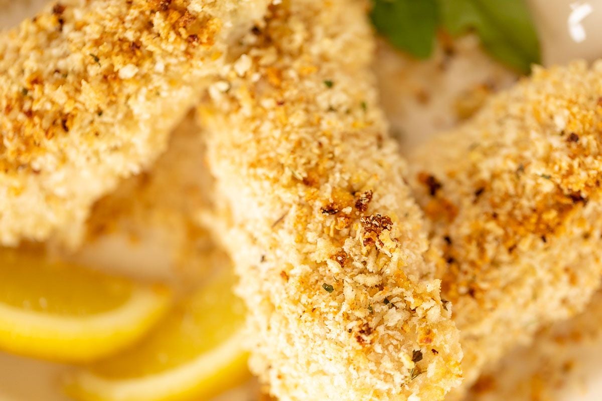 A white platter with panko breaded chicken, sliced lemon for garnish