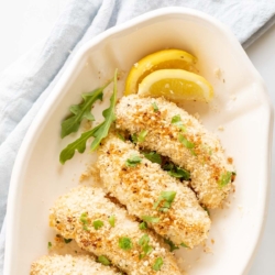 A white platter with panko chicken tenders, sliced lemon for garnish