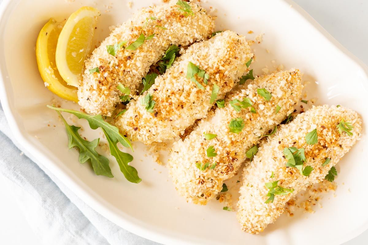 A white platter with panko chicken tenders, sliced lemon for garnish