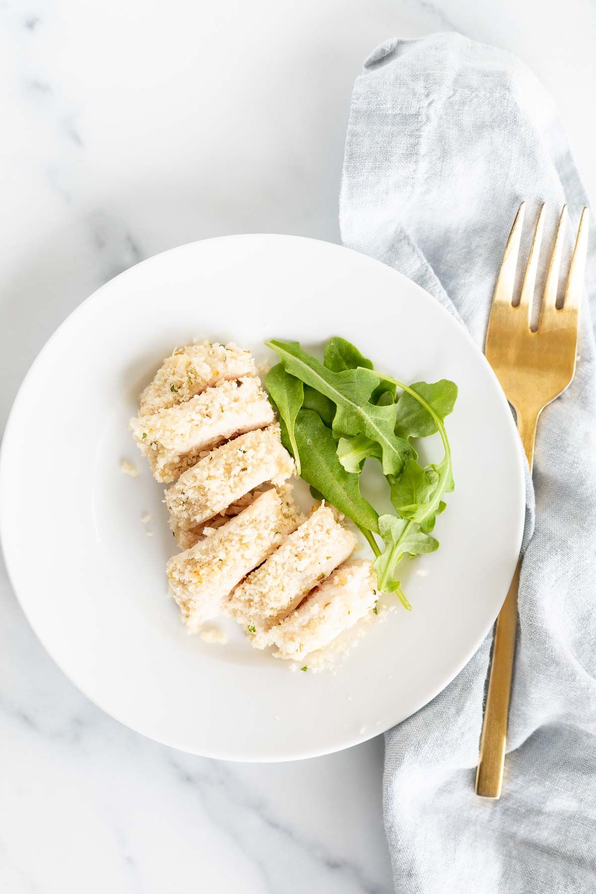 A white plate with a piece of panko chicken, greens on the side