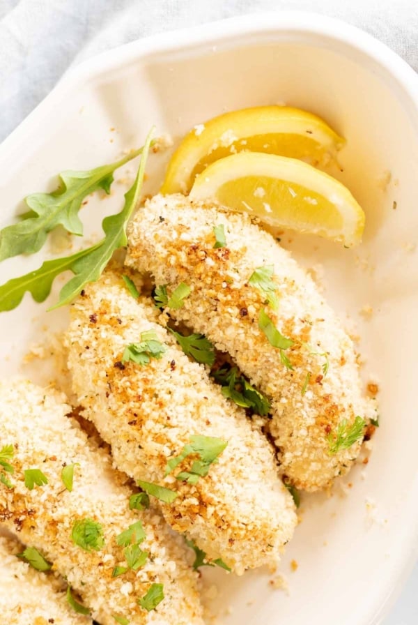 A white platter with panko chicken tenders, sliced lemon for garnish