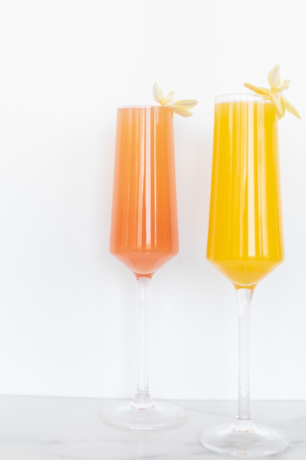 Two prosecco mimosas, garnished with white flowers on a white background