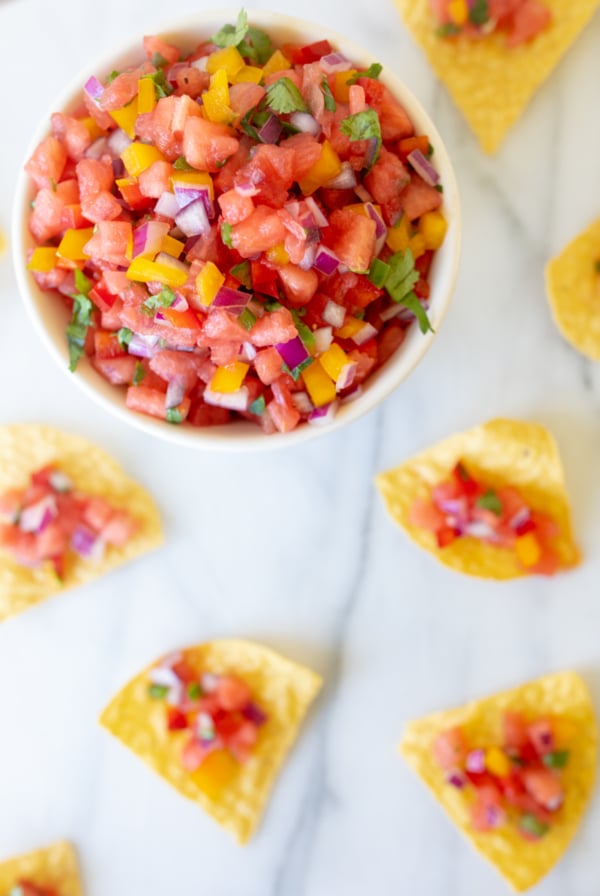 A bowl of fresh tomato salsa recipes surrounded by tortilla chips on a marble surface.