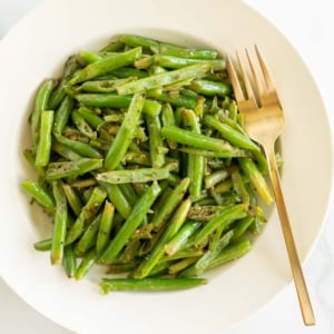 A white plate full of seasoned green beans as a steak side dish