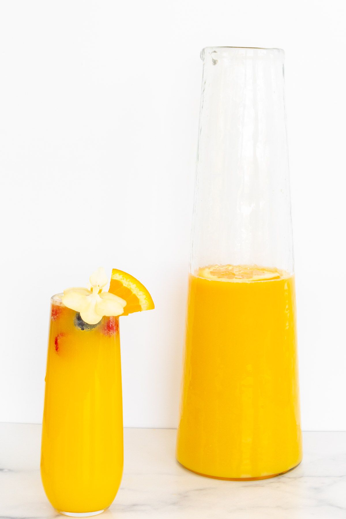 A champagne glass with a mimosa, bottomless mimosa pitcher to the side