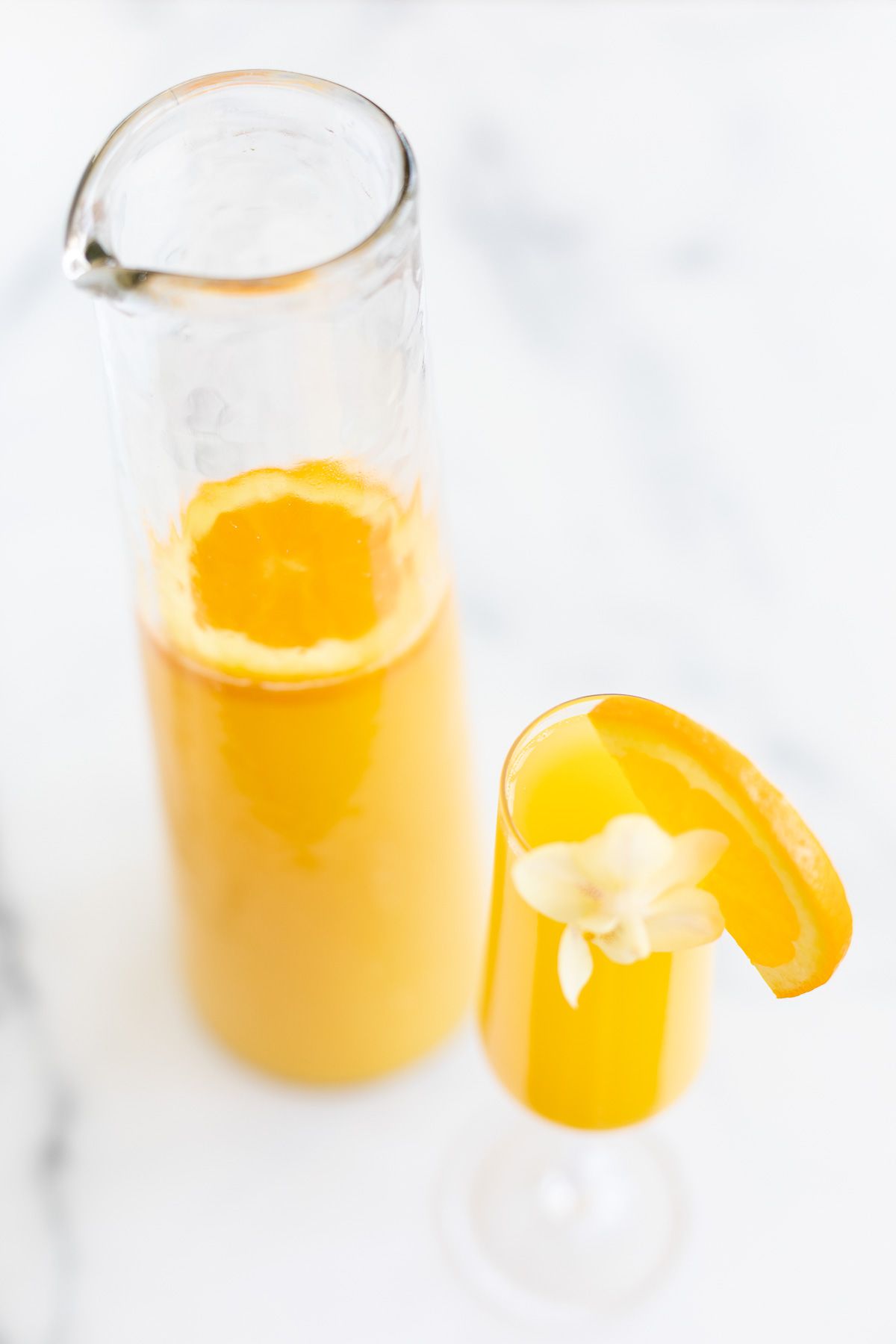 A mimosa in a champagne glass, pitcher of mimosas to the side