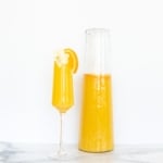 A glass pitcher of bottomless mimosas with a single flute of a mimosa to the side