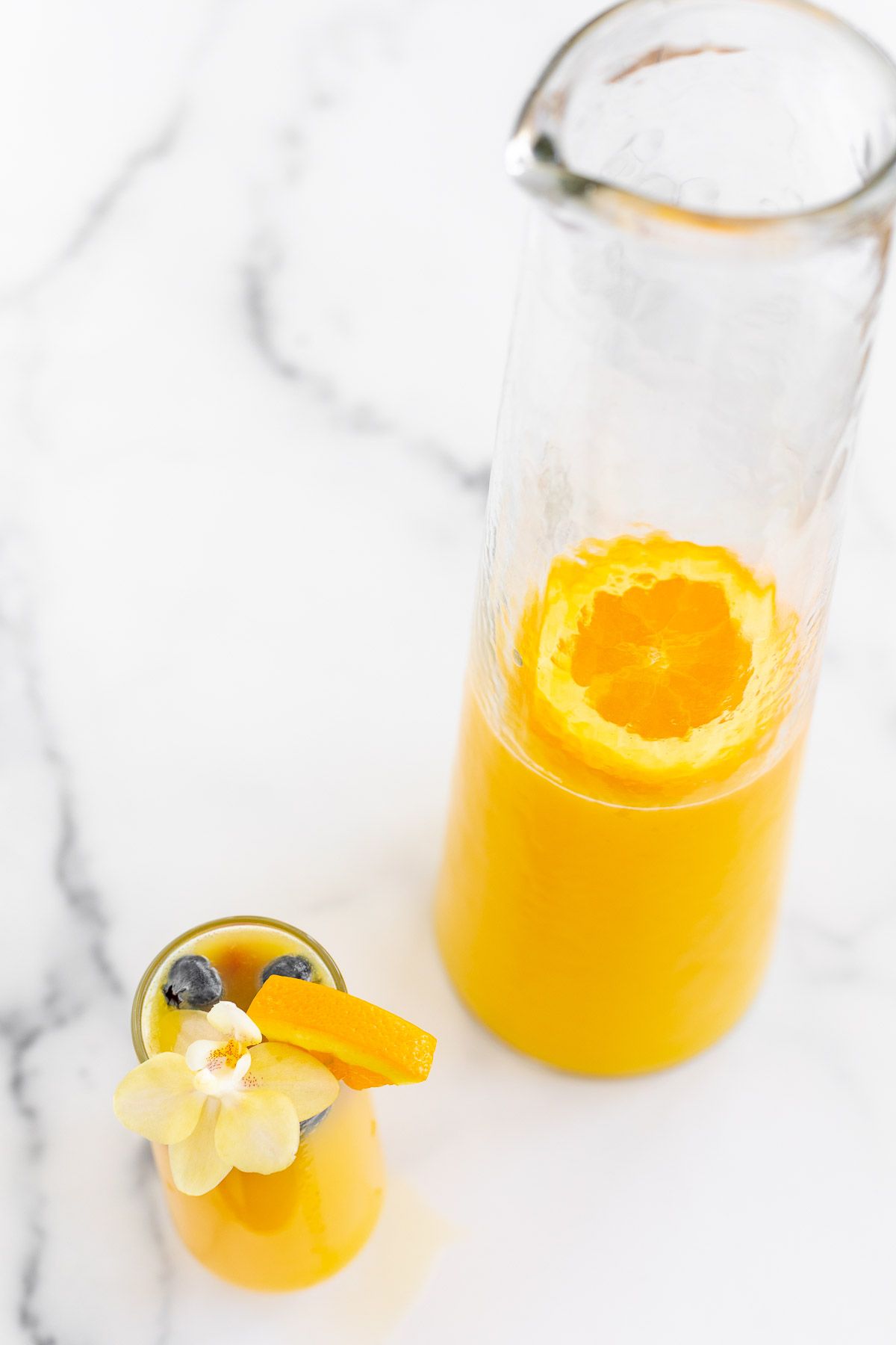 A champagne glass with a mimosa, bottomless mimosa pitcher to the side
