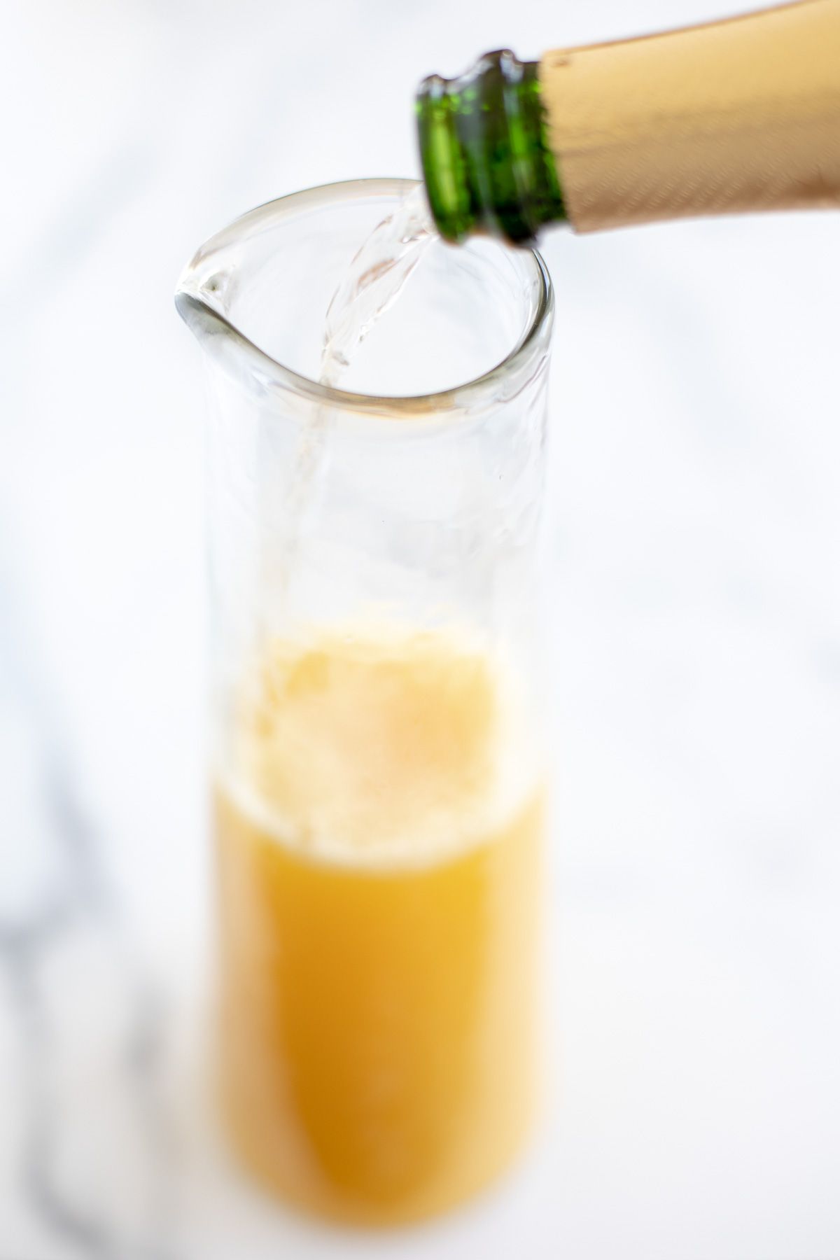 Prosecco pouring into a glass pitcher of bottomless mimosas