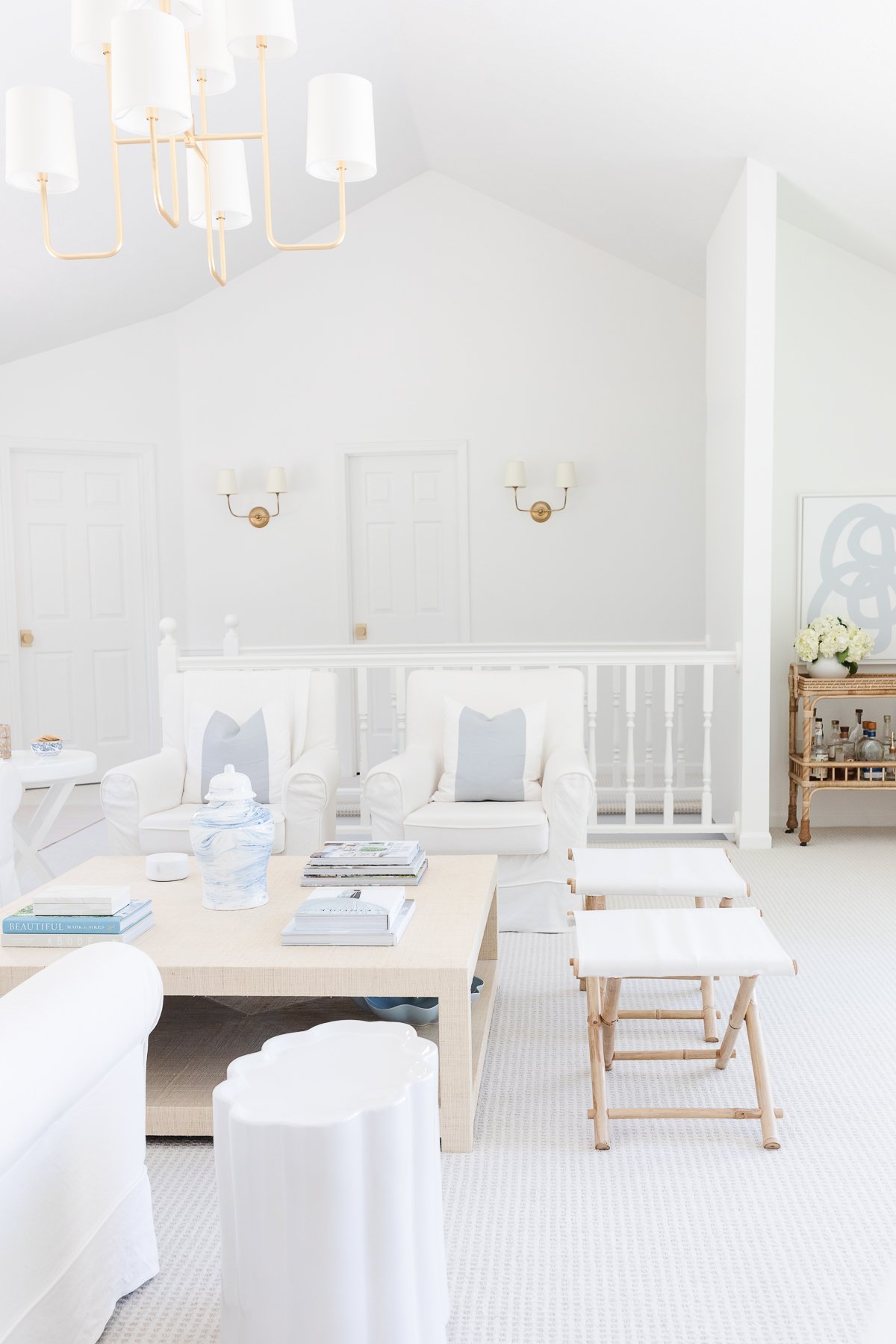 A white living room with a chandelier and ceramic stools.