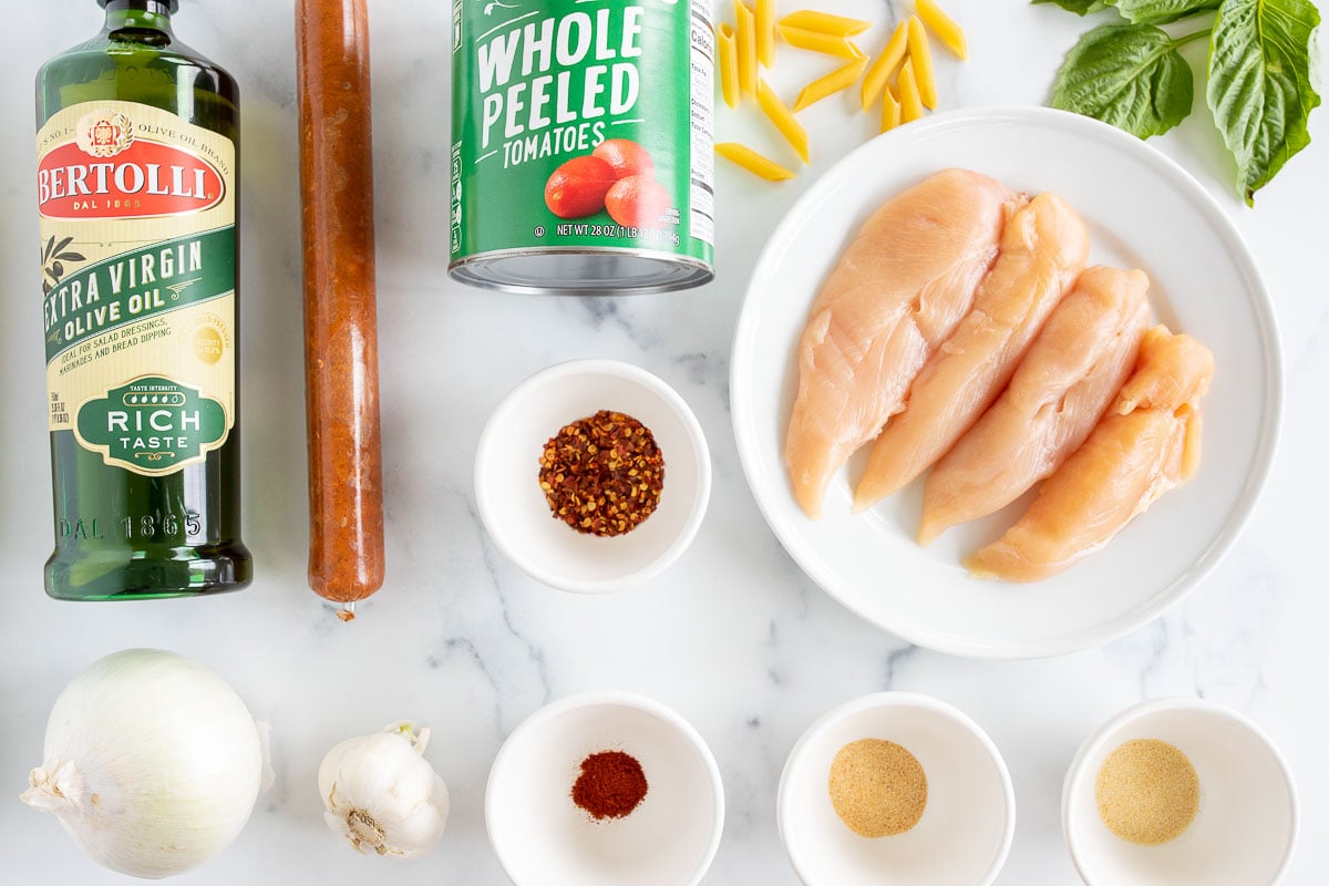 Ingredients for chicken and chorizo pasta laid out on a marble countertop.
