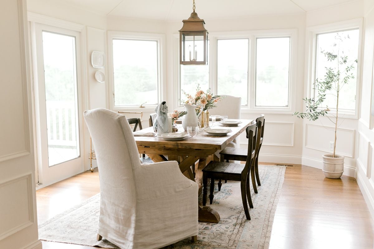 A farmhouse dining table surrounded by wood chairs in a white dining room