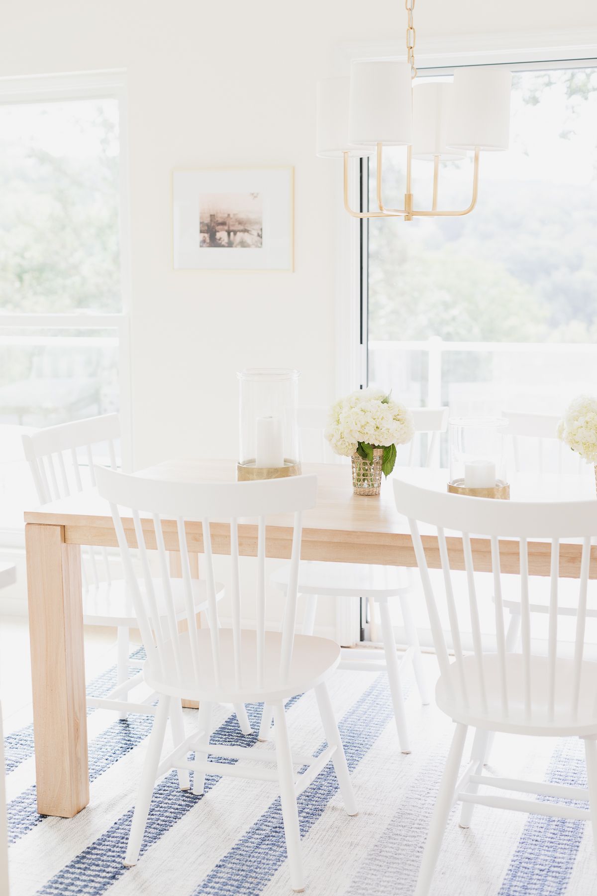 A teak dining table with white chairs on a blue and white striped rug