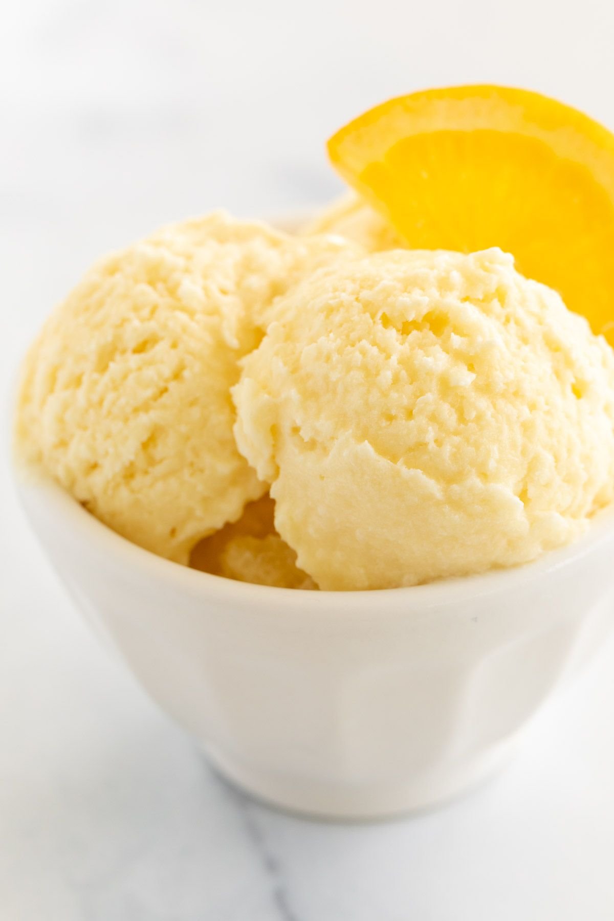 orange sherbet garnished with a slice of orange in a white bowl