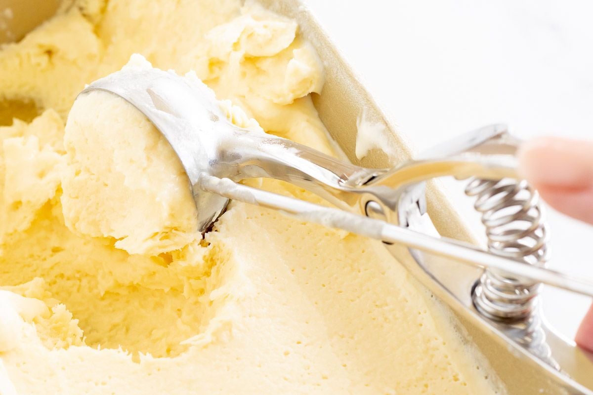 Homemade orange sherbet in a gold loaf pan, with an ice cream scoop