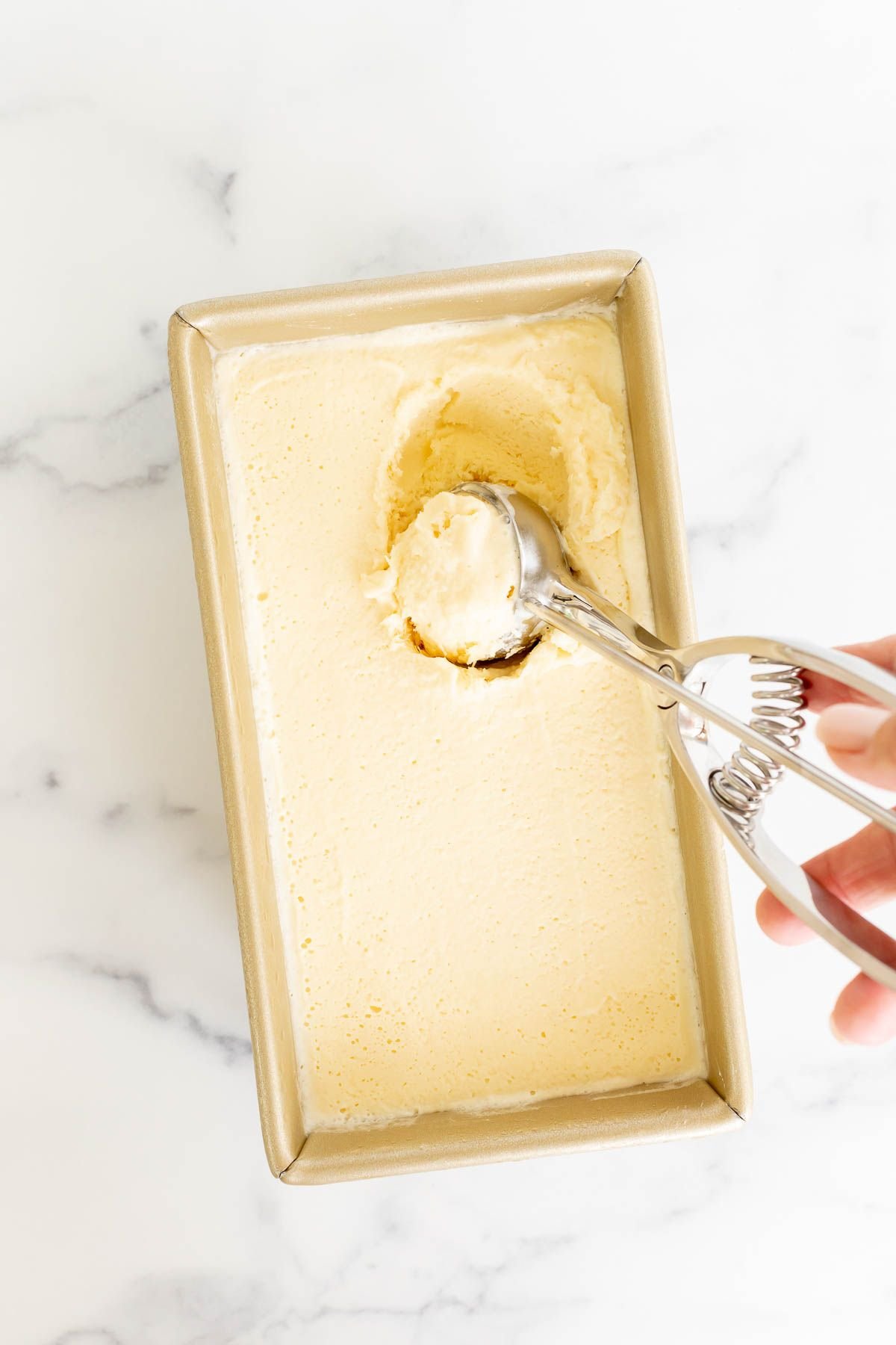 Homemade orange sherbet in a gold loaf pan, with an ice cream scoop