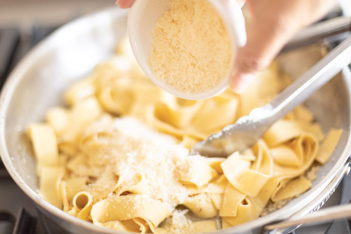 parmesan being added to a silver pan of noodles