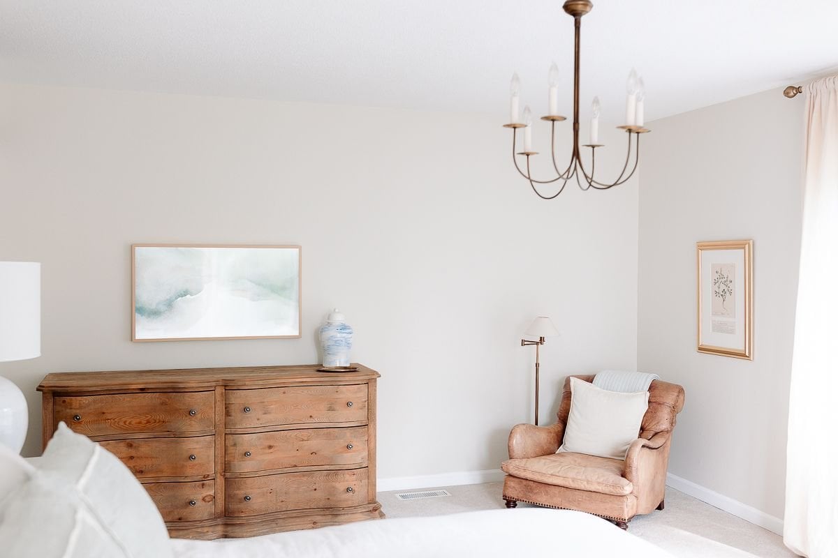 A white bedroom with a wood RH dresser and a leather chair in the corner