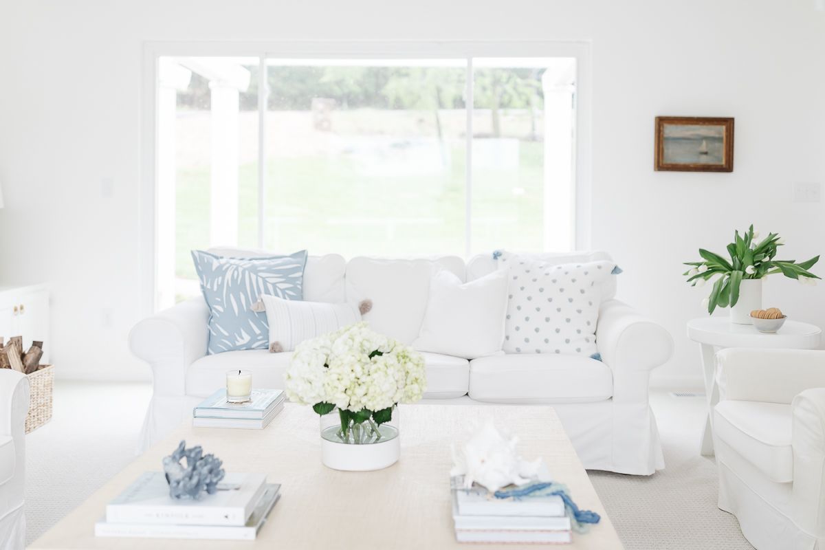 A bright white living room with a white slipcovered sofa and light blue pillows