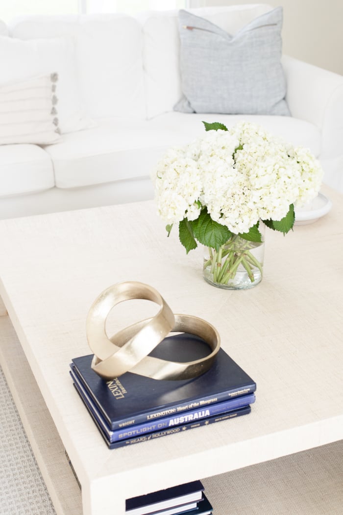 A raffia coffee table with navy blue books and fresh flowers. 