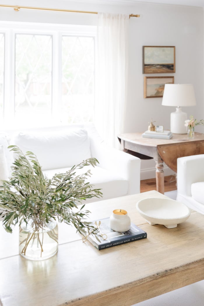 A wood coffee table in a white room with natural, neutral coffee table decor. 