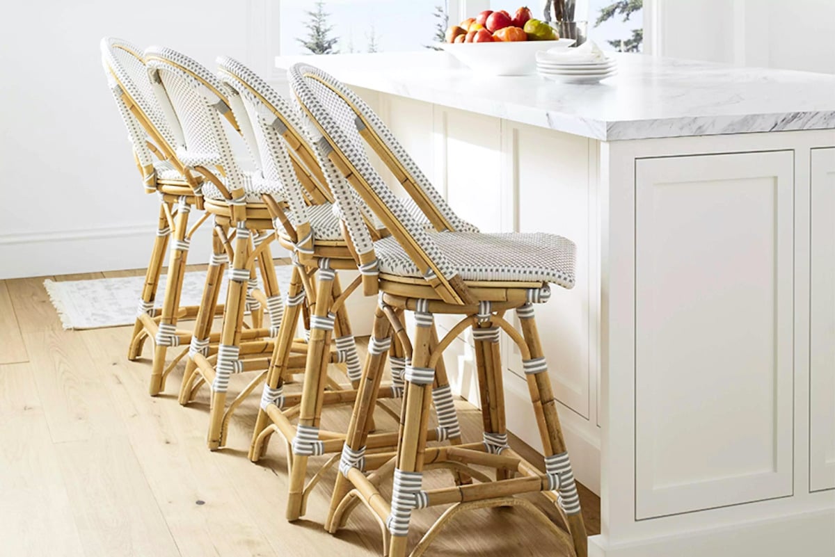 Four rattan bar stools complement the white kitchen.