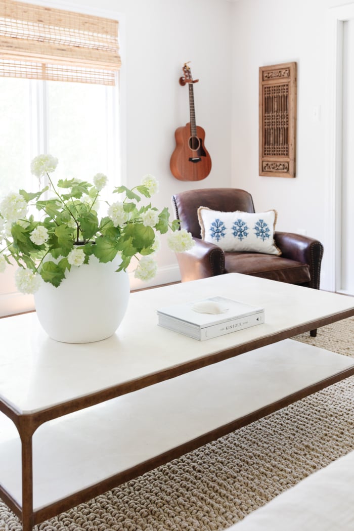 A brass and marble coffee table with simple coffee table decor like a vase of flowers and a stack of books. 