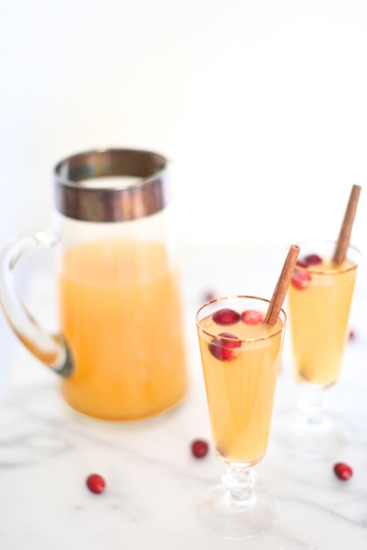 Two glasses of cranberry punch with cinnamon sticks and apple slices.