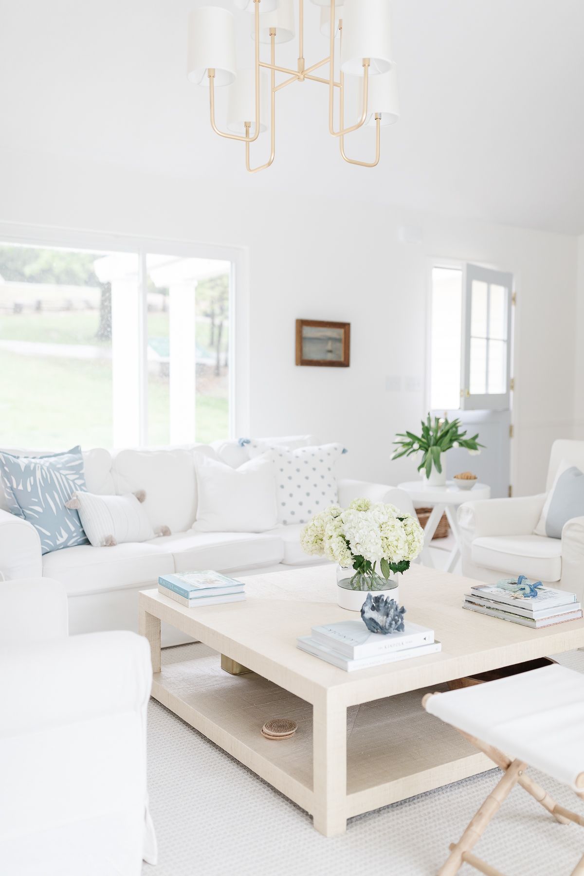 A coastal inspired white living room with a beige linen square coffee table in the center.